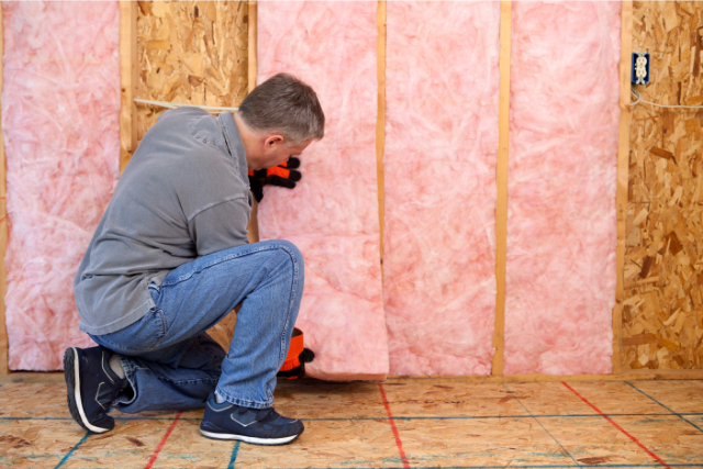 Worker installing fiberglass insulation in a home.